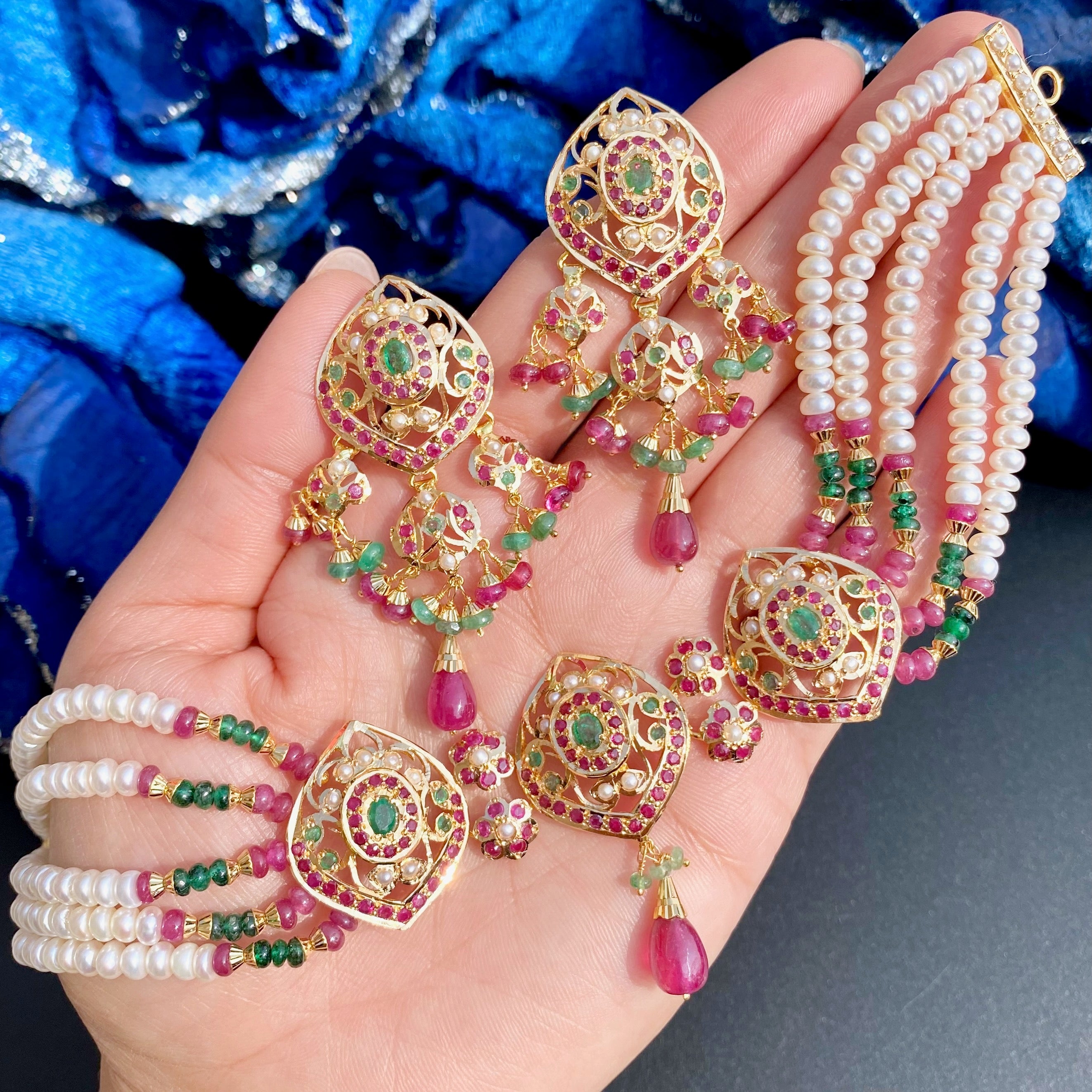 Gold jewelry set with earrings and necklaces on a hand against a blue floral background